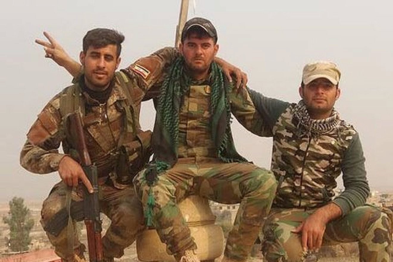 Assyrian Christian pose in front a newly erected cross atop the Mar Shmony church in the liberated town of Bartella, Iraq. Credit: Nineveh Plains Protection Unit.