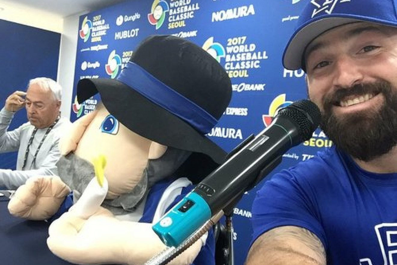 Cody Decker (right), a member of Team Israel at the World Baseball Classic (WBC), poses with the Israeli team’s mascot—the Hanukkah toy Mensch on a Bench (center)—at a WBC press conference in March. Credit: Cody Decker via Twitter.