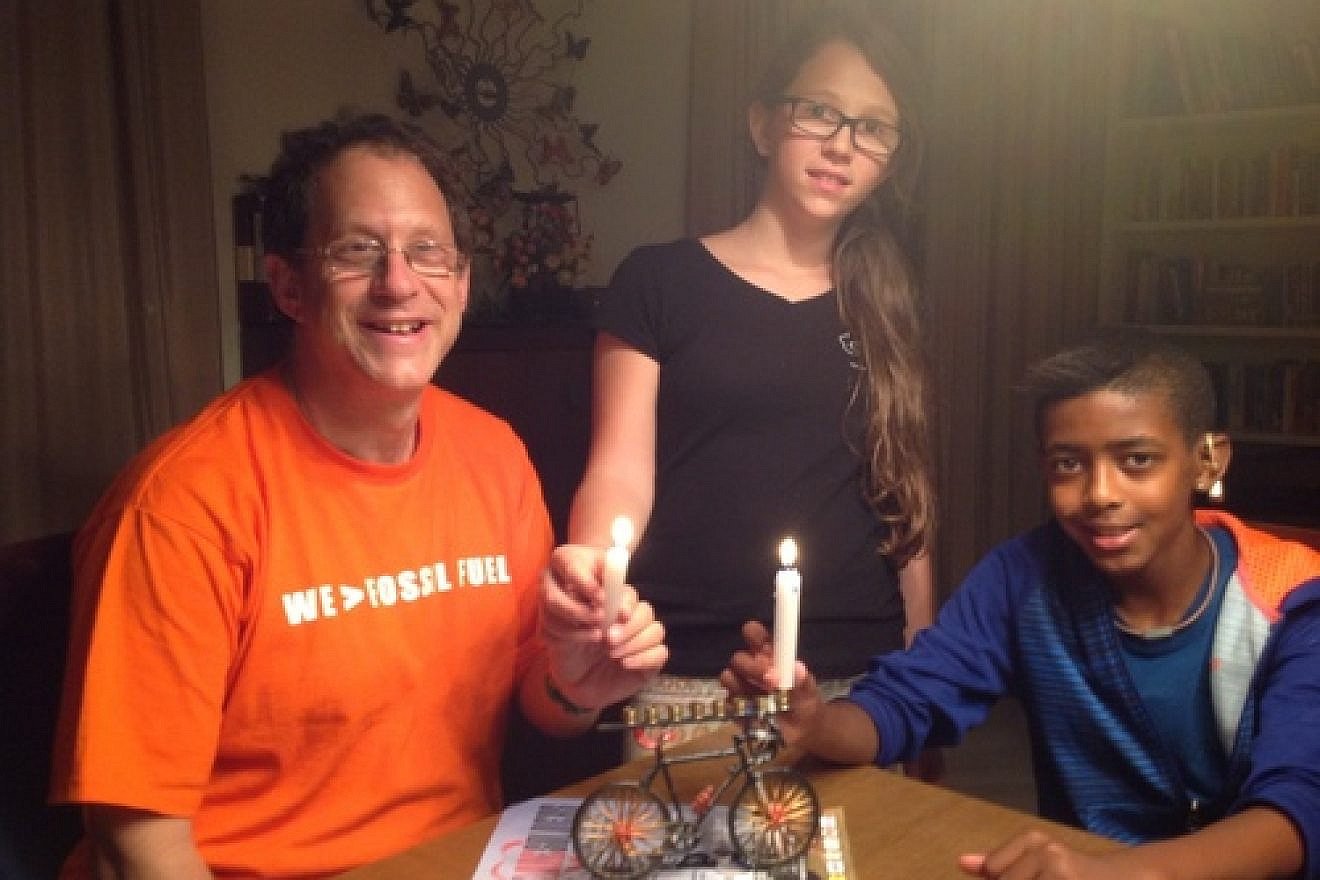 Solar-power pioneer Yosef Abramowitz (left) pictured with two of his five children, Ashira and Zamir, as the family uses its bicycle-shaped Hanukkah menorah. Credit: Courtesy Yosef Abramowitz.