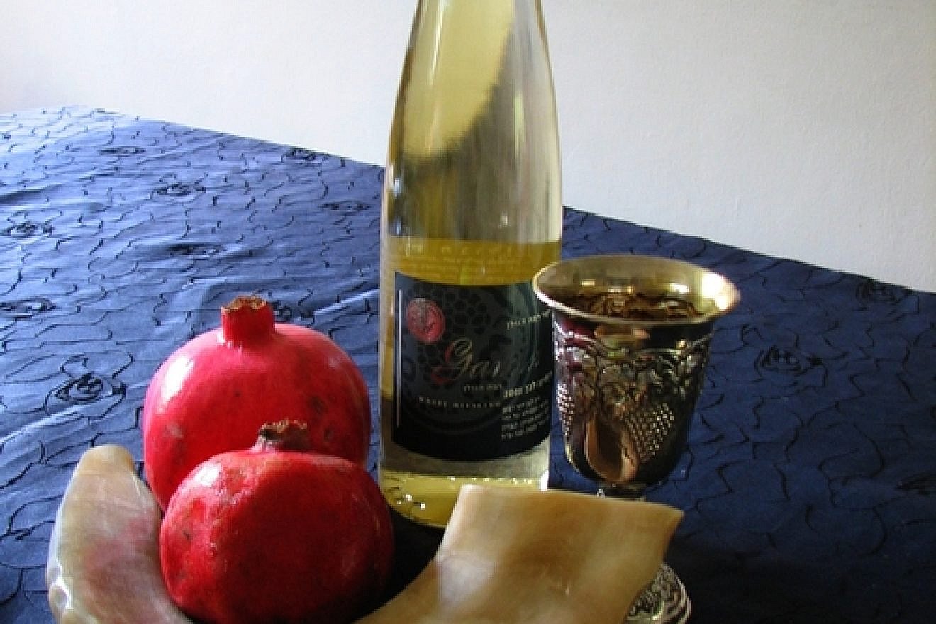Symbols of Rosh Hashanah, the Jewish New Year, including the shofar, an apple and honey, pomegranates, wine and a silver Kiddush cup. Credit: Gilabrand via Wikimedia Commons.