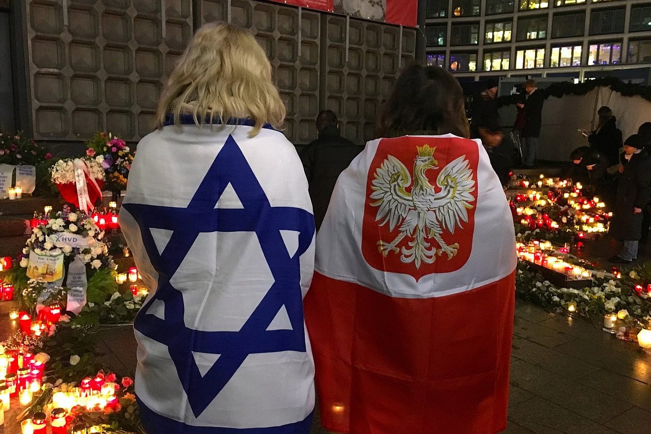 Antje Böttinger (left), wrapped in an Israeli flag, and a woman wearing a Polish flag visit a memorial to victims of the December 2016 Berlin Christmas market terror attack, Dec. 19, 2018. Credit: Orit Arfa.