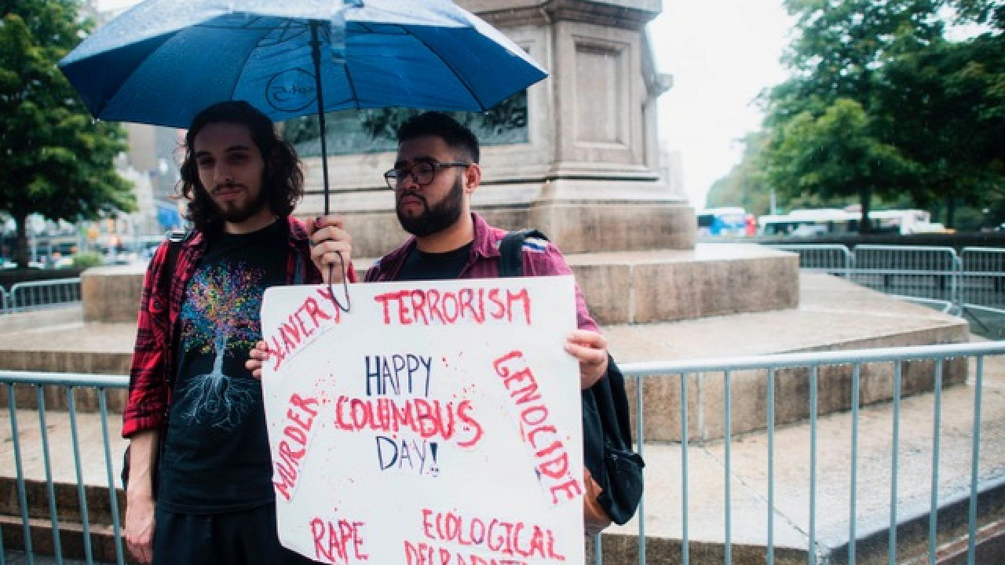 Two protesters display a placard under the statue of Christopher Columbus at the Columbus Circle in New York on Oct. 9, 2017, calling for the removal of the statue. Credit: JEWEL SAMAD/AFP/Getty Images.