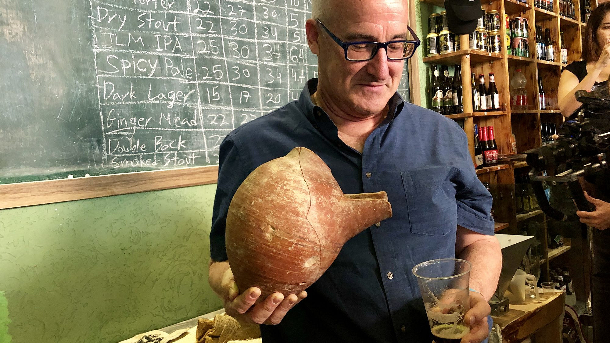 Professor Aren Maeir, from Bar-Ilan University’s Land of Israel studies and archaeology, models an ancient vessel and the new, recreated beer. Credit: Eliana Rudee.