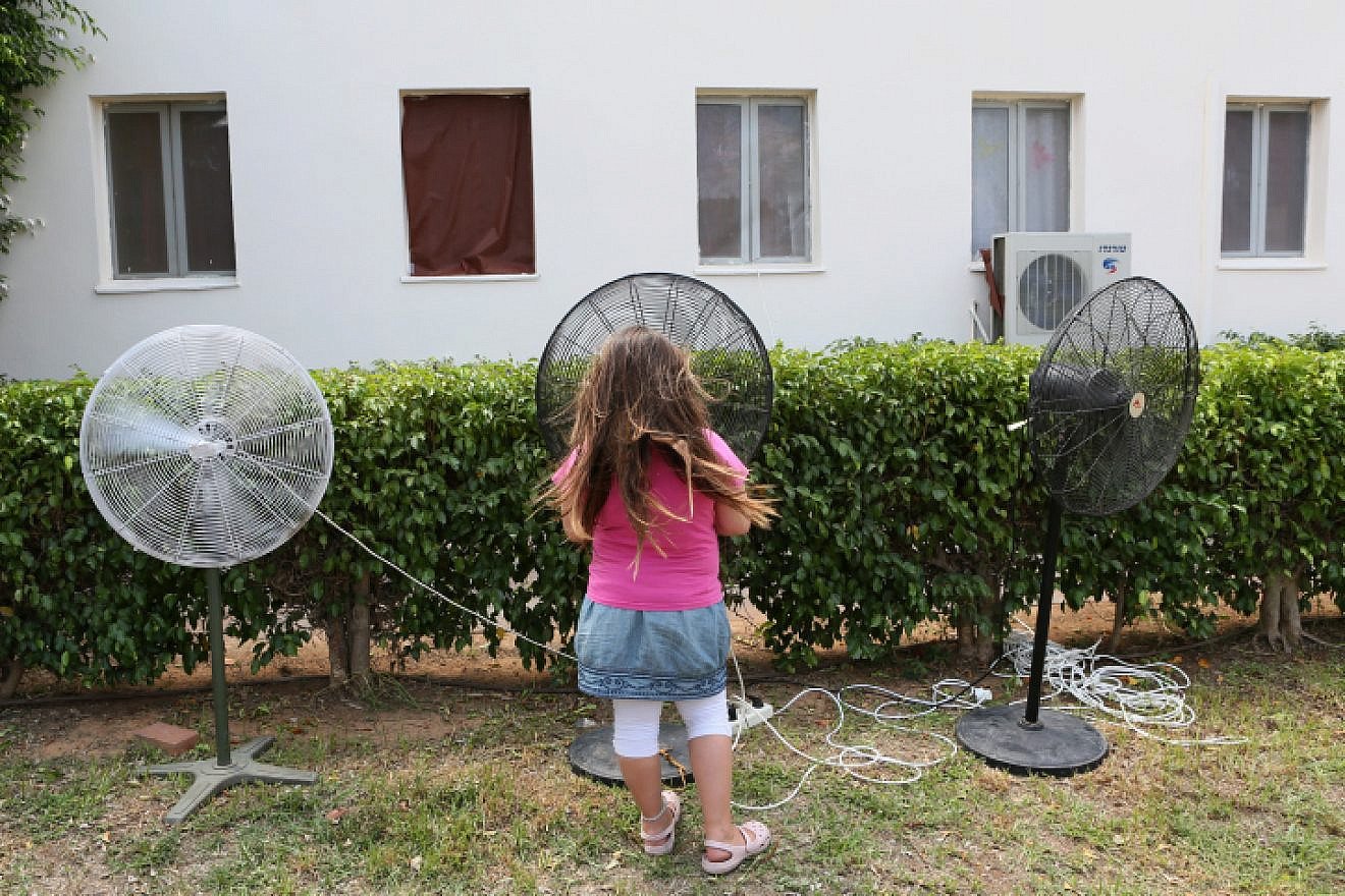 A young girl cools herself on a hot summer day by standing next to fans at the Zitan yishuv, on Aug. 15, 2012. Photo by Nati Shohat/Flash90.