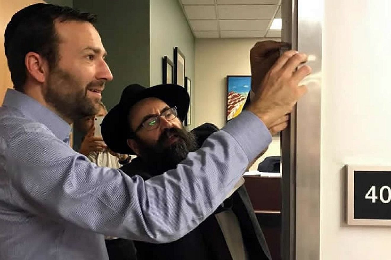 California State Sen. Ben Allen, author of the state's landmark “Mezuzah Bill,” and Rabbi Mendy Cohen of Chabad of Sacramento, Calif., affix a “mezuzah” on Allen's office door after passage of the legislation. Credit: Legislative Jewish Caucus via Chabad.org/News.