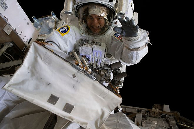 NASA astronaut Jessica Meir waves at the camera during a spacewalk with fellow NASA astronaut Christina Koch (out of frame). They ventured into the vacuum of space for seven hours and 17 minutes to swap a failed battery charge-discharge unit (BCDU) with a spare during the first all-woman spacewalk, Oct. 18, 2019. Credit: NASA via Wikimedia Commons.