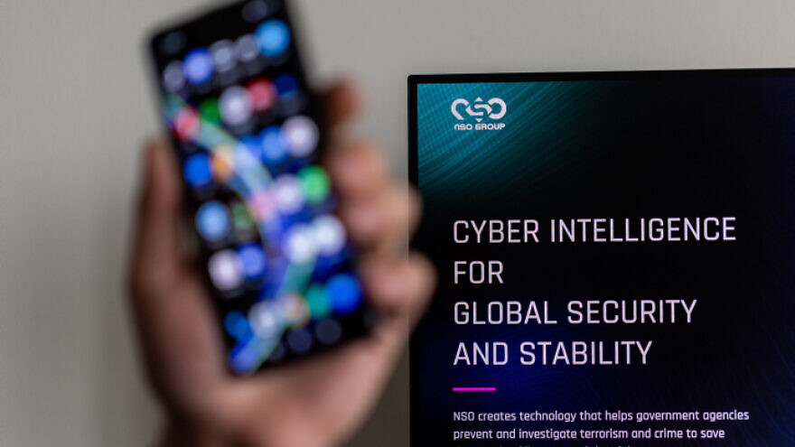 An Illustration of a man holding his phone with NSO GROUP logo on a computer screen at the background, in Jerusalem, on February 7, 2022. Photo by Yonatan Sindel/Flash90.