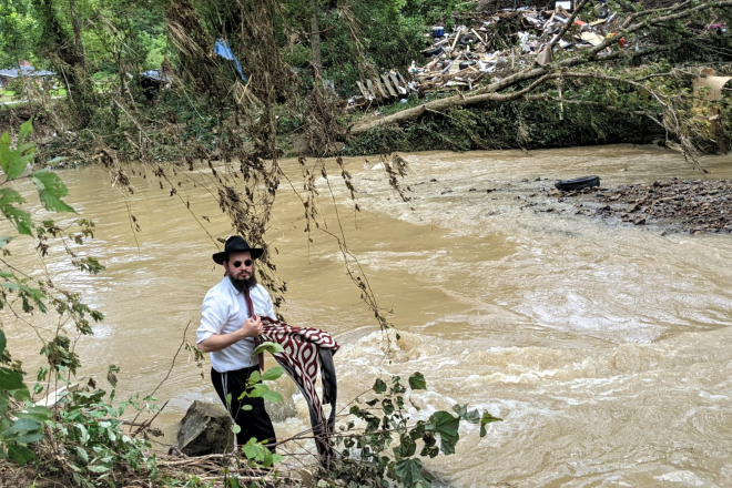 During a stop to deliver an aid package and a word of comfort, Rabbi Shlomo Litvin helped clear debris from the river bordering a home damaged in the flood. Credit: Courtesy of Chabad of Kentucky.