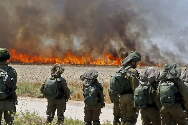 Israeli soldiers walk amidst smoke from a fire in a wheat field near the Kibbutz of Nahal Oz, along the border with the Gaza Strip, on May 14, 2018 which was caused by incendiaries tied to kites flown by Palestinian protesters from across the border.
Dozens of Palestinians were killed by Israeli fire on May 14 as tens of thousands protested and clashes erupted along the Gaza border against the US transfer of its embassy to Jerusalem, after months of global outcry, Palestinian anger and exuberant praise from Israelis over President Donald Trump's decision tossing aside decades of precedent. / AFP PHOTO / JACK GUEZ