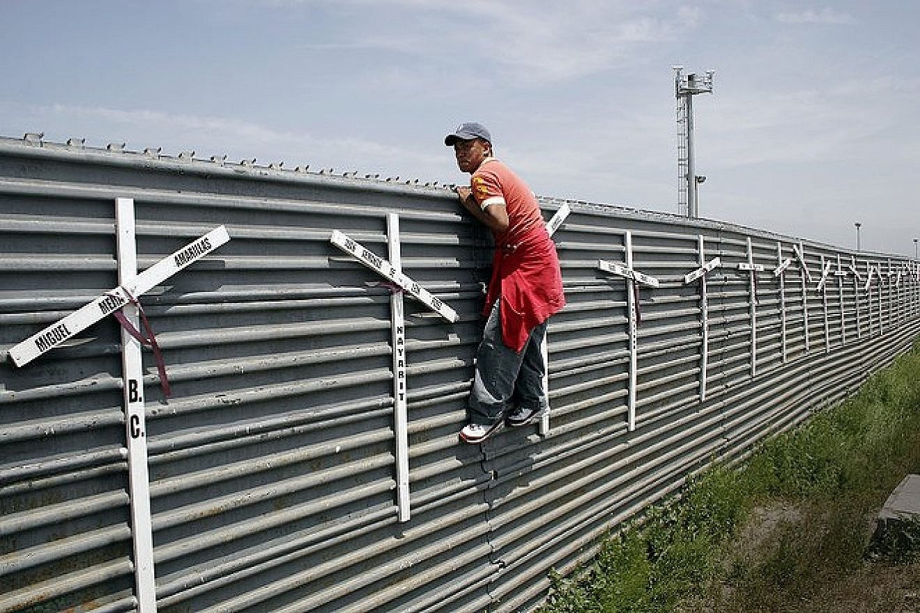 A migrant from Mexico scaling the border fence into the United States. Source: Wikimedia Commons.