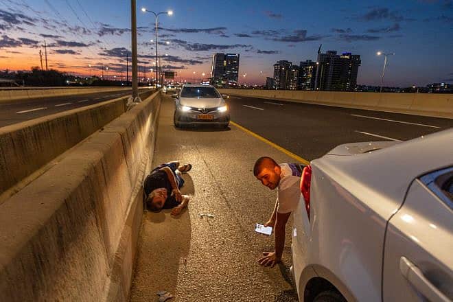 Israelis take cover by the side of a highway as a siren warns of incoming rockets, Oct. 17, 2023. Photo by Yossi Aloni/Flash90.