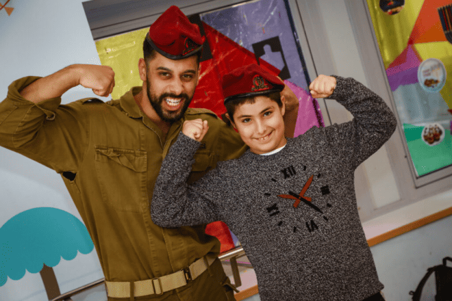 A member of the Israel Defense Forces visits a Chai Lifeline kid at Shaare Zedek Medical Center in Jerusalem. Credit: Courtesy of Chai Lifeline.