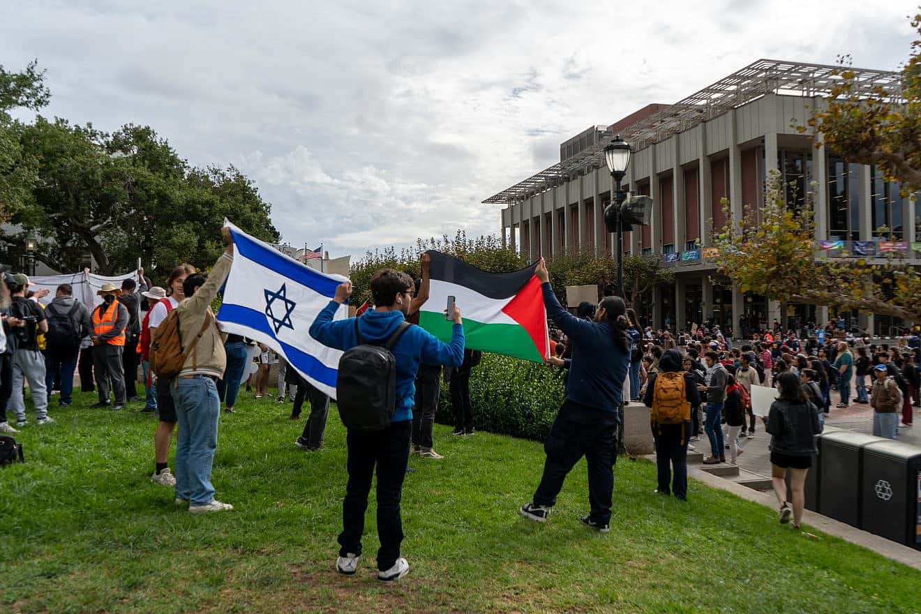 At a protest at the University of California, Berkeley, two pro-Israel protesters hold up an Israeli flag while two pro-Palestinian protesters stand in front of it with a Palestinian flag on Oct. 25, 2023. Credit: Kefr4000 via Wikimedia Commons.
