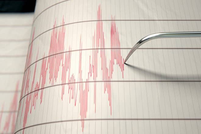 A close-up of a seismograph machine needle drawing a red line on graph paper depicting seismic and earthquake activity. Credit: Inked Pixels/Shutterstock.