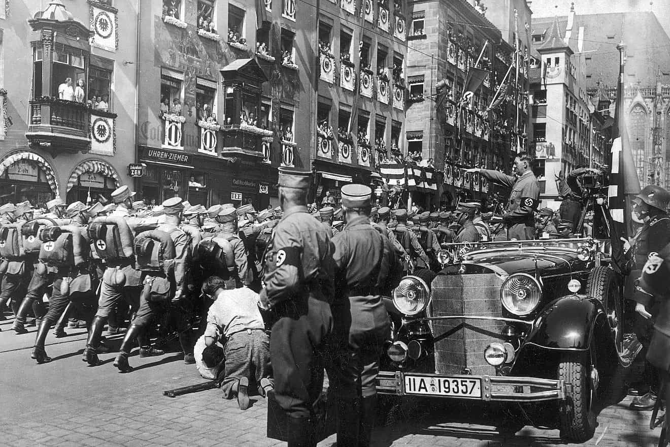 Adolf Hitler standing in his Mercedes-Benz 770 reviewing SA (Sturmabteilung) members in a parade during the Nuremberg rally, the sixth Nazi Party Congress held in Nuremberg attended by about 700,000 Nazi Party supporters, Sept. 5-10, 1934. Hitler is accompanied by the Blutfahne, (“Blood Flag,” ceremonial swastika flag) and its bearer SS-Sturmbannführer Jakob Grimminger. Credit: Narodowe Archiwum Cyfrowe, the National Digital Archives of Poland via Wikimedia Commons/Public Domain.
