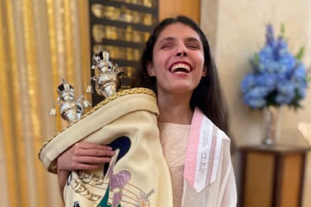 A young JBI patron with vision impairment happily celebrates while holding a Torah. Credit: Courtesy.