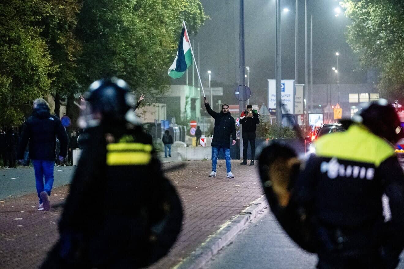 A supporter waves a Palestinian flag in front of police officers during a pro-Palestinian demonstration on the sideline of the UEFA Europa League football match between Ajax Amsterdam and Maccabi Tel Aviv, in Amsterdam on Nov. 7, 2024. Photo by Jeroen Jumelet/ANP/AFP via Getty Images.