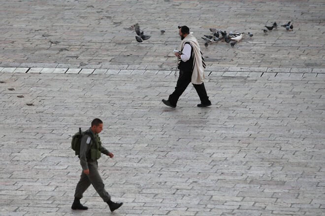 An Orthodox man walks along the Western Wall plaza, passing an Israeli soldier in the Old City of Jerusalem. Photo by Keren Freeman/Flash90.