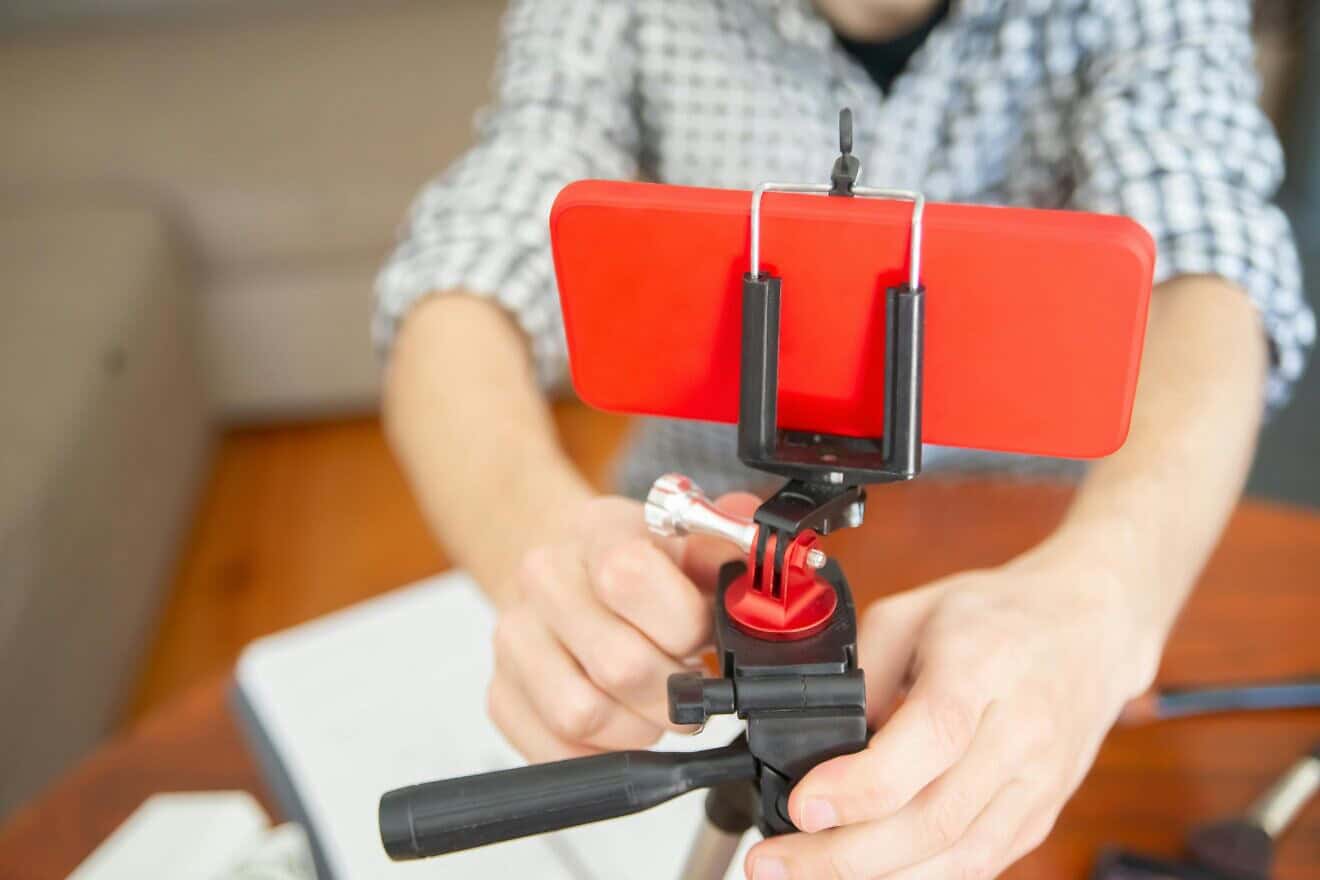 A person holding a smartphone on a tripod. Photo by Kampus Production/Pexels.