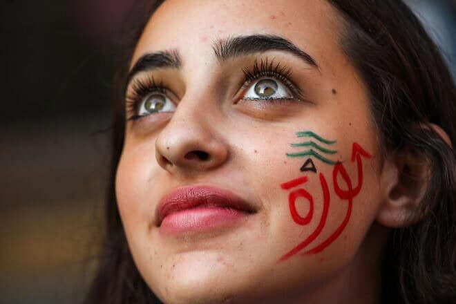 A woman wearing face paint depicting a Lebanese cedar tree and the Arabic word “revolution” looks on during a demonstration on the sixth day of protest against tax increases and official corruption in the center of the capital Beirut's downtown district on Oct. 22, 2019. Photo by Anwar Amro/AFP via Getty Images.