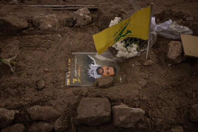 A picture of a terrorist and a Hezbollah flag lie on a temporary grave as civilians and terrorists are exhumed for relocation  in Tyre, Lebanon, on Dec. 4, 2024. Photo by Ed Ram/Getty Images.