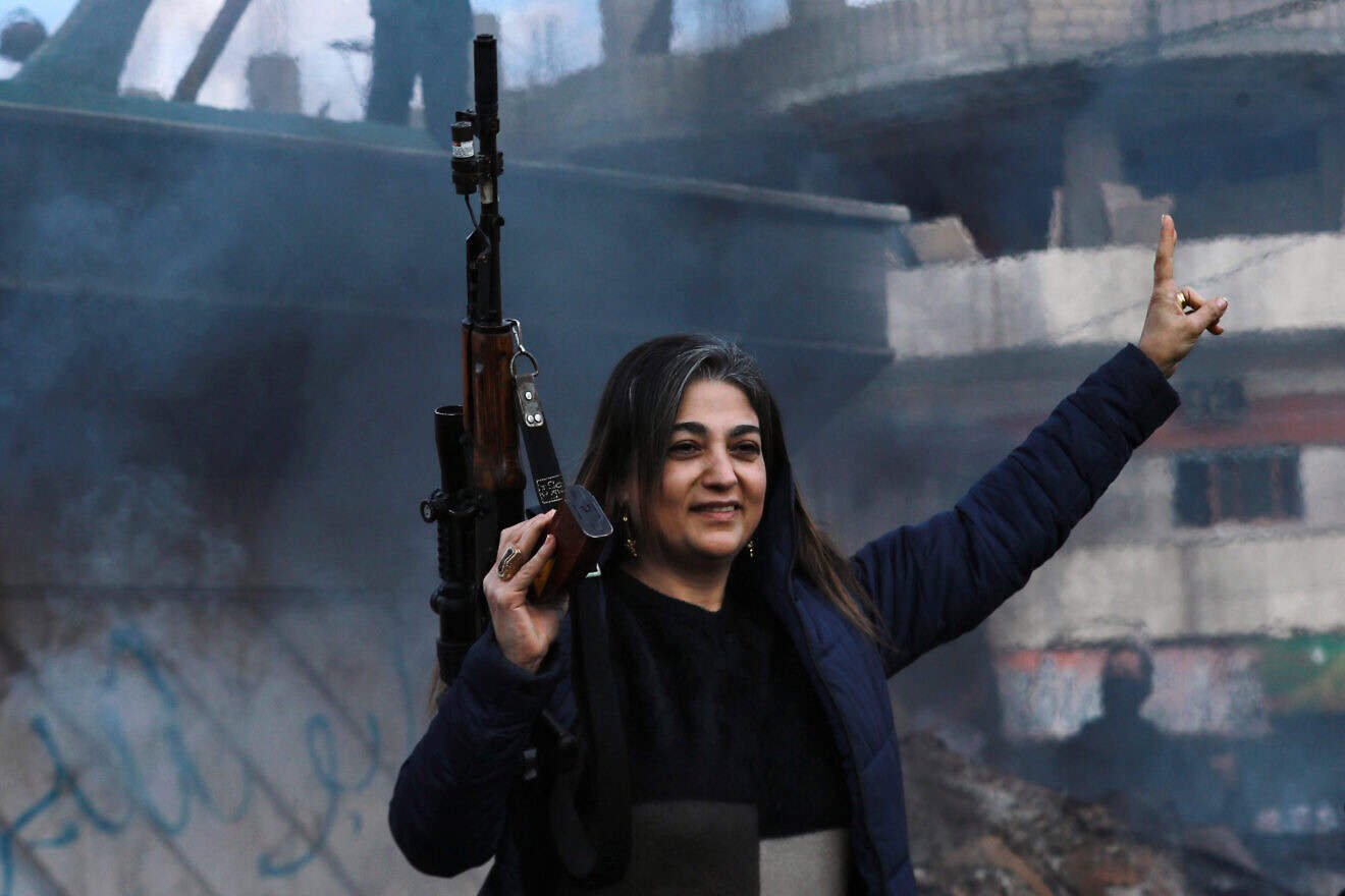 An armed woman flashes the V for victory sign as Syrian Kurds celebrate the fall of capital Damascus to anti-government fighters, in the city of Qamishli on Dec. 8, 2024. Photo by Delil Souleiman/AFP via Getty Images.