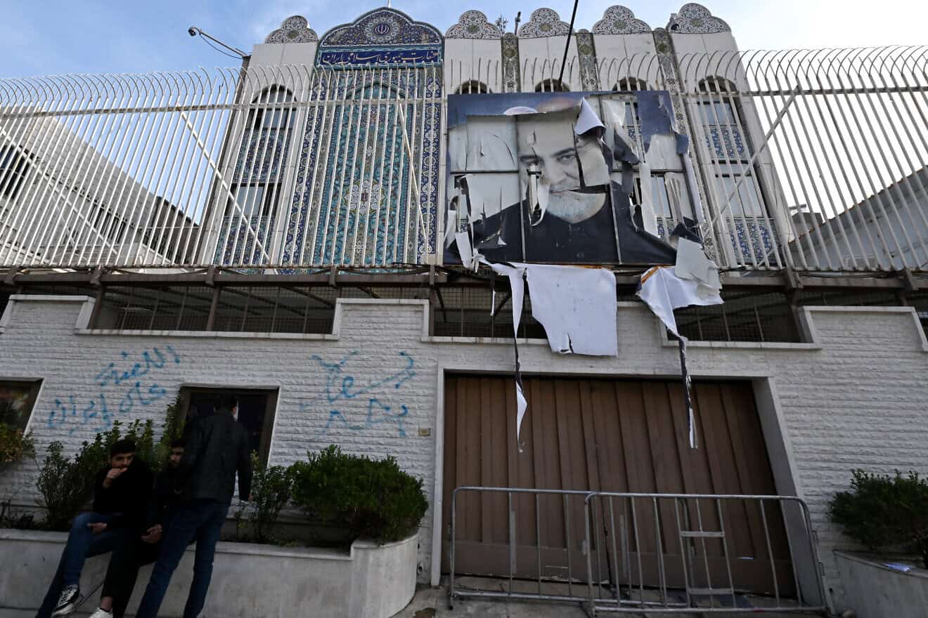 Young Syrians sit outside Iranian embassy, which was ransacked after anti-government fighters took Damascus the previous day, with a portrait of Iran's slain Revolutionary Guards commander Qassem Soleimani still hanging on its fence, in the Syrian capital on Dec. 9, 2024. Photo by Louai Beshara/AFP via Getty Images.