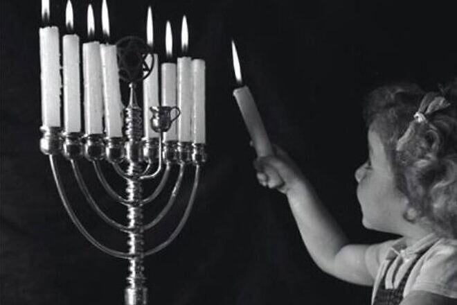 A girl in Jerusalem, representing the young generation of Jewish life in Eretz Israel, lights a Chanukah menorah in 1947 as a symbol of the revival of light. Credit: KKL-JNF Photo Archive.