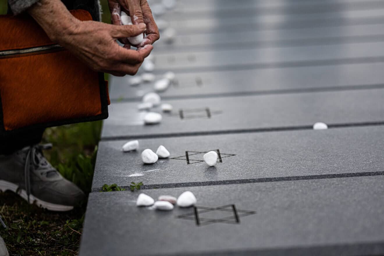 A woman places white visitation stones on a grave marker at Stuttgart Army Airfield in Filderstadt, Germany, 2023. Credit: U.S. Army USAG-S by Marcus Fichtl, public domain via Wikimedia Commons.