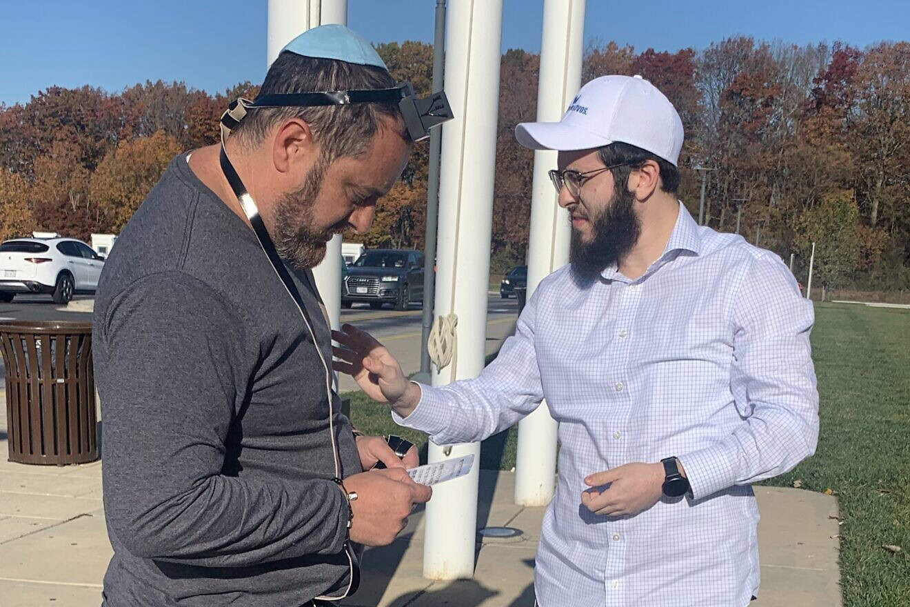 Rabbi Mendel Grossbaum helps a man put on tefillin at a rest stop before a rally for Israel, on Nov. 14, 2023. Photo by Faygie Holt.