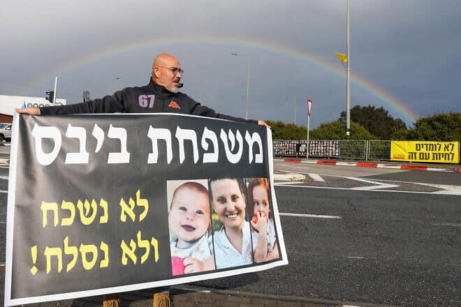 A man in northern Israel holds a banner showing members of the Bibas family—mom Shiri, and children Ariel and Kir—who were murdered by Hamas in the Gaza Strip after being taking from their home on Oct. 7, 2023, in the Hamas-led terrorist attacks in southern Israel, Feb. 20, 2025. Photo by Ayal Margolin/Flash90.