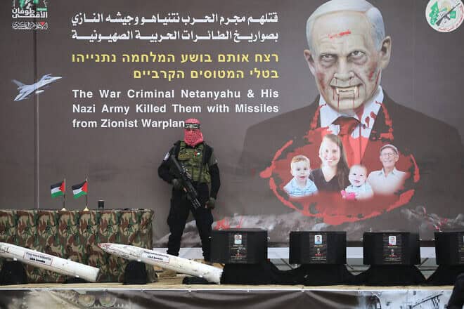 A Hamas terrorist stands in front of a banner bearing an altered portrait of Israel's prime minister and the Bibas family, on stage ahead of the handing over the bodies of four Israeli hostages in Khan Yunis in the southern Gaza Strip on Feb. 20, 2025. Photo by Eyad Baba/AFP via Getty Images.