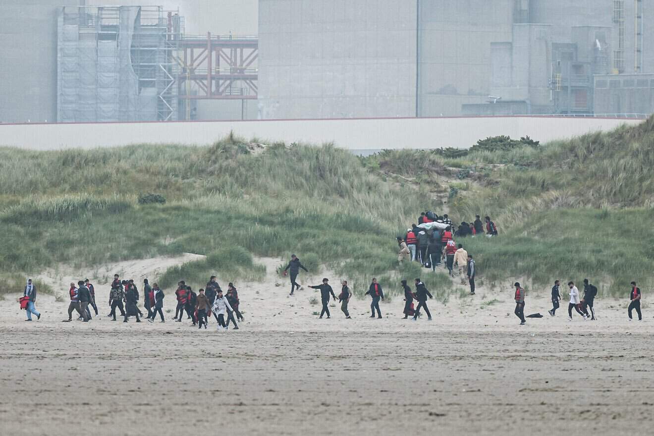 Migrants run up the dunes near Gravelines Nuclear Power Station to hide the smuggling boats from French National Police dispatched to prevent them from illegally crossing the English Channel to Britain in Gravelines, northern France, on June 12, 2023. Photo by Sameer al-Doumy/AFP via Getty Images.