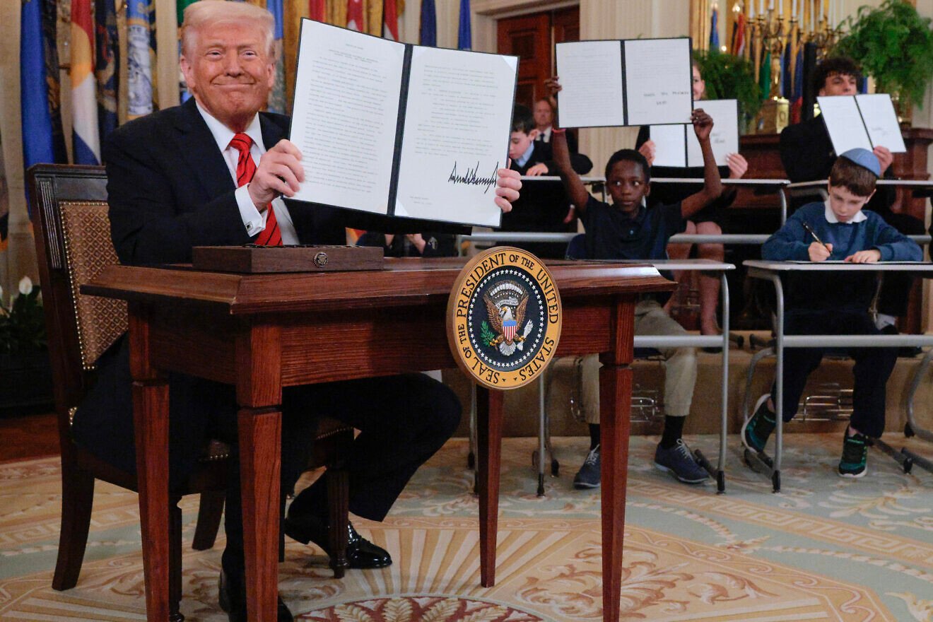 Joined by children seated at school desks, U.S. President Donald Trump holds up the signed executive order to reduce the size and scope of the Education Department during a ceremony in the East Room of the White House on March 20, 2025 in Washington, DC. Photo by Chip Somodevilla/Getty Images.