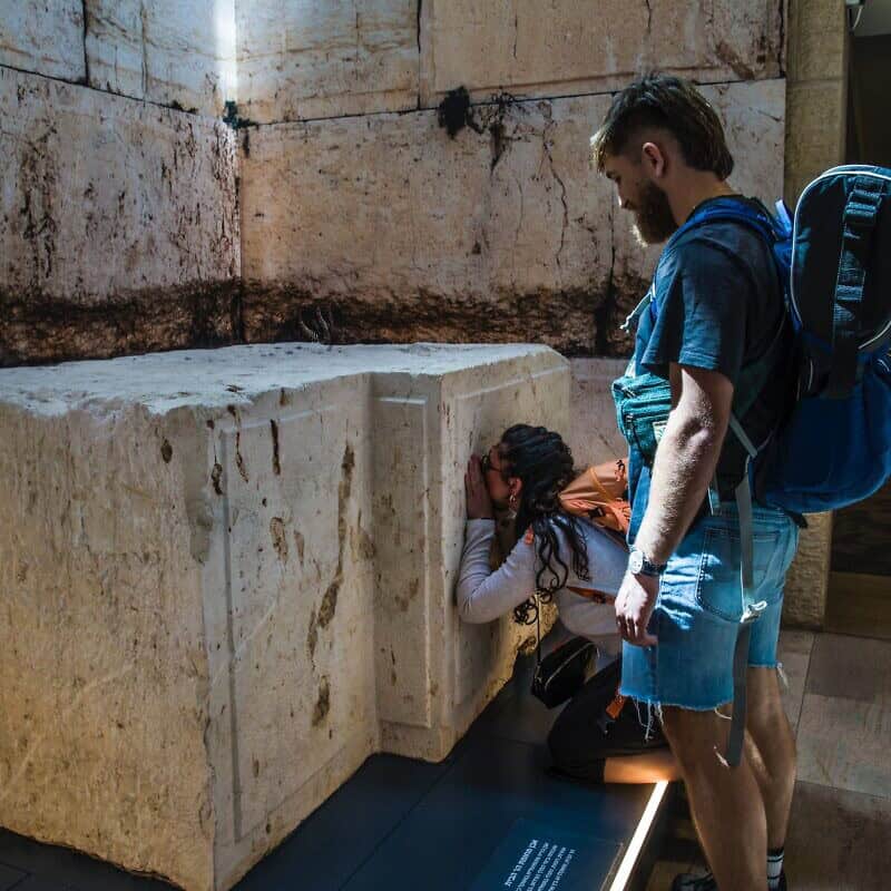 Shelly Sarah, a 22 year old Israeli from Hadera, stops at the Western Wall stone on display at Israel's Ben-Gurion International airport before a trip to Thailand as her boyfriend looks on, March 25, 2025. Credit: Rina Castelnuovo.