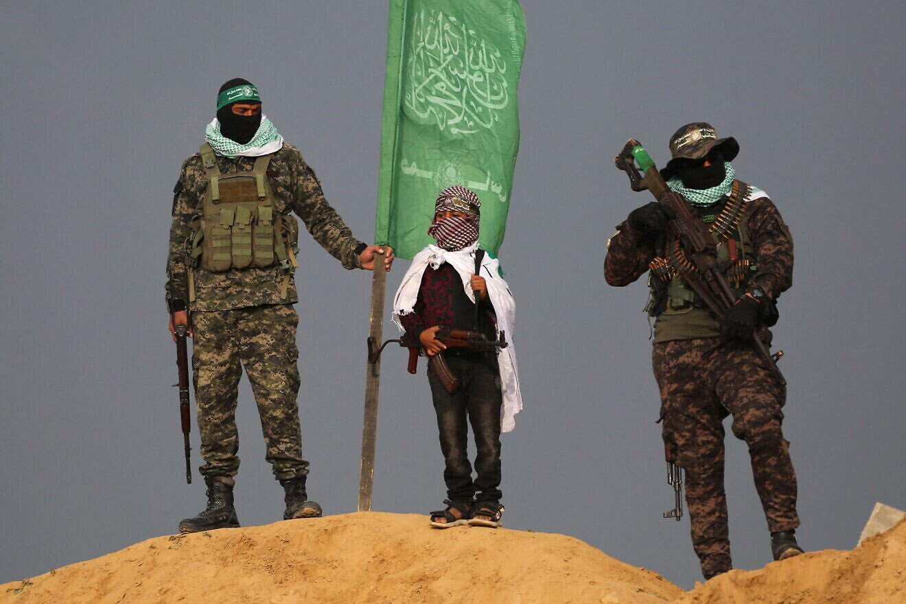 A Palestinian masked child holds a rifle as he stands between two Hamas militants at the site where the bodies of four Israeli hostages were handed over to the Red Cross in Khan Yunis in the southern Gaza on Feb. 20, 2025. Photo by Eyad Baba/AFP via Getty Images.