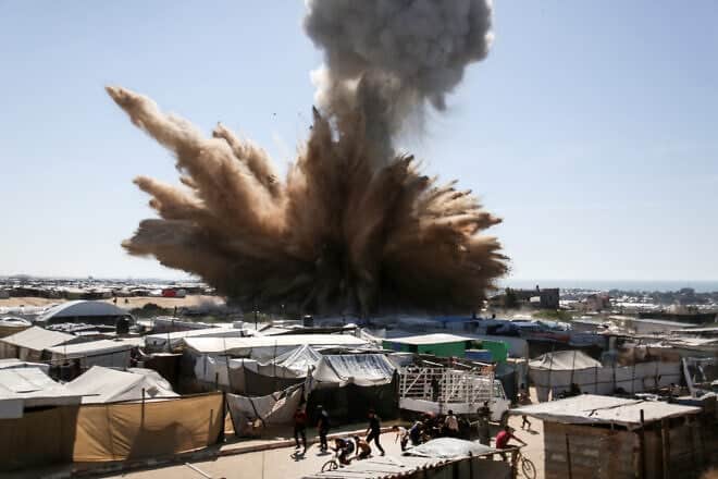 People run for cover as a plume of smoke rises above tents at a camp for displaced Palestinians in northern Khan Yunis in the southern Gaza Strip, during an Israeli strike on April 19, 2025. Photo by AFP via Getty Images.