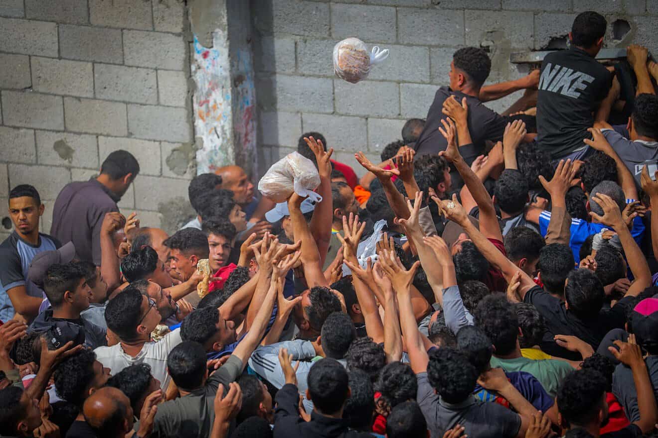 Gazans reach out for bags of pitas being distributed through a bakery window in the Nusseirat camp, in the central Strip, May 22, 2025. Photo by Ali Hassan/Flash90.