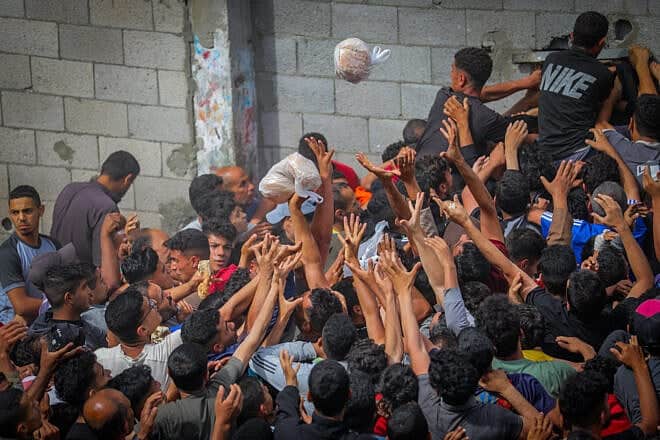 Gazans reach out for bags of pitas being distributed through a bakery window in the Nusseirat camp, in the central Strip, May 22, 2025. Photo by Ali Hassan/Flash90.
