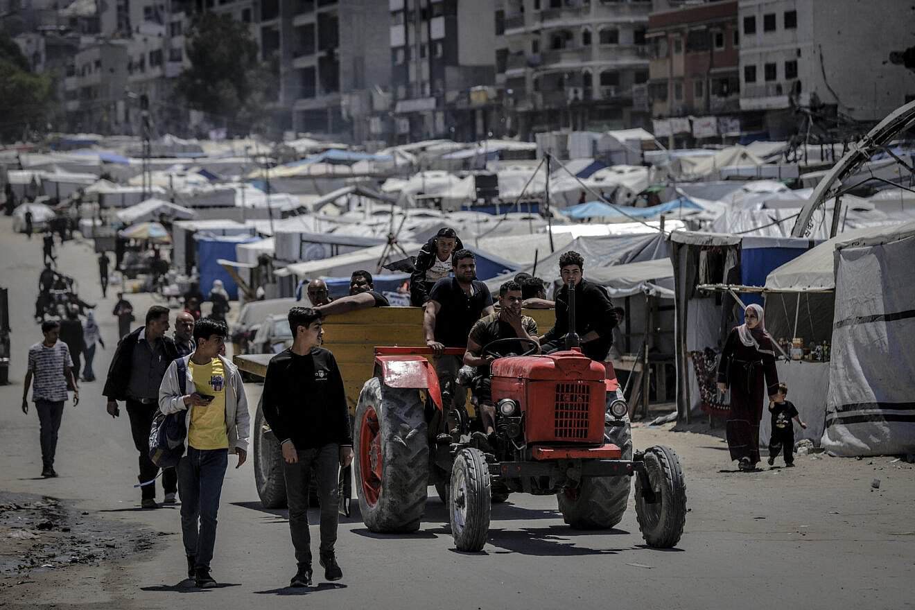 A man drives a red tractor past pedestrians and tents lining the street in the Al-Rimal neighborhood of Gaza City, on May 4, 2025. Photo by Saeed Jaras/Middle East Images/AFP via Getty Images.