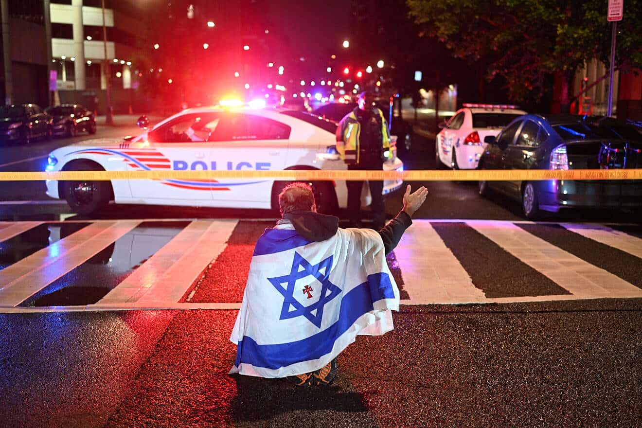 A man draped in the Israeli flag, bearing a cross and the name "Jesus" at its center, gestures as Metropolitan Police officers secure the area outside the Capital Jewish Museum following a shooting that left two people dead in Washington, DC, in the early hours of May 22, 2025. Two Israeli embassy staffers were shot dead late Wednesday, May 21, outside a Jewish museum in Washington by a gunman who shouted "free Palestine," authorities said, with US officials and Israeli diplomats expressing shock and outrage over the killings. Photo by Alex Wroblewski/AFP via Getty Images.