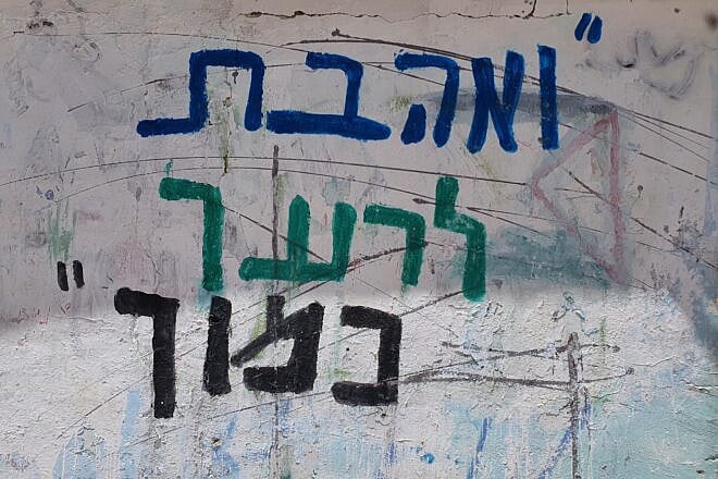 Hebrew graffiti on a wall in Jerusalem that says, "Love your neighbor as yourself." Credit: Korenn via Wikimedia Commons.