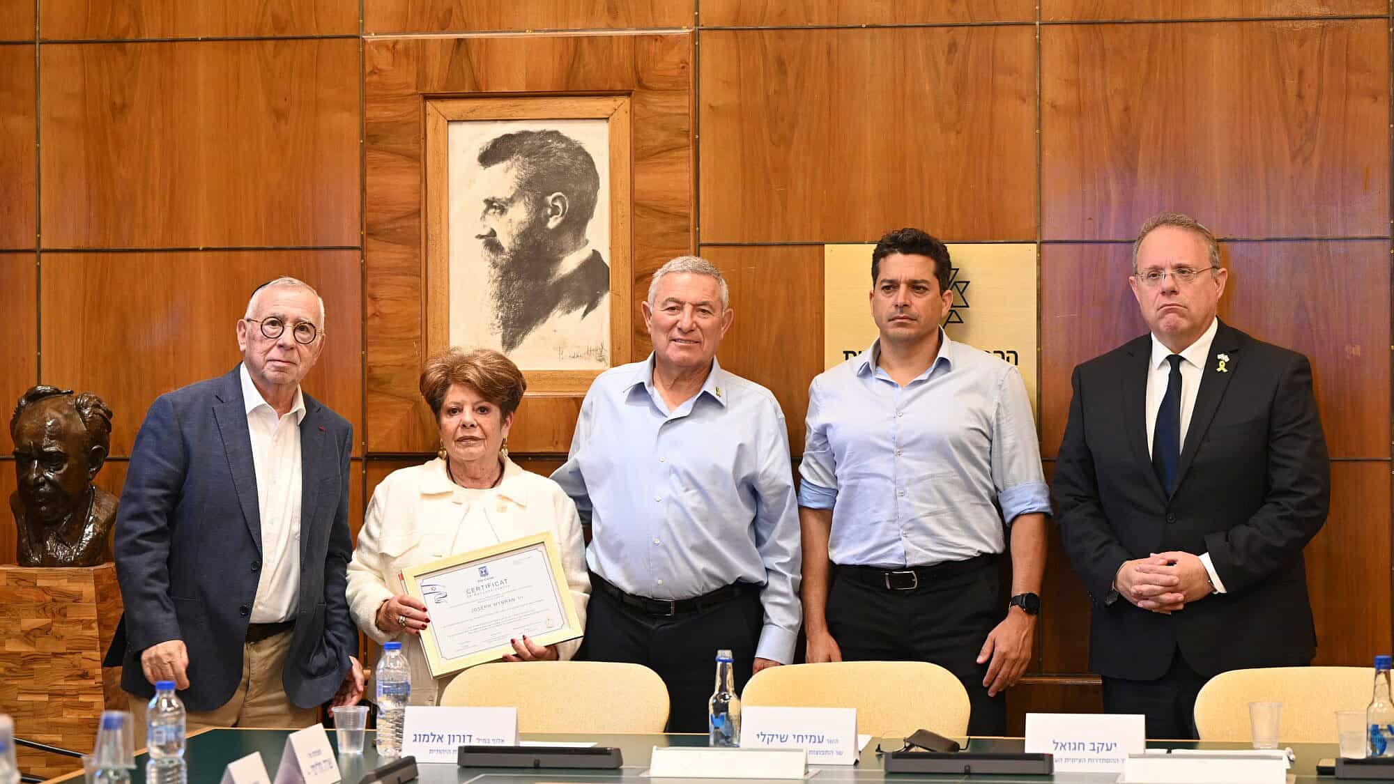 Jewish Agency chairmnan Doron Almog (center), flanked by Diaspora and Combating Antisemitism Minister Amichai Chikli (center-right) and World Zionist Organization chairman Yaakov Hagoel (far right), presents a certificate in memory of Dr. Joseph Wybran to his widow, Emmy Wybran-Sosnovski (center-left) and lifelong friend Jacques Heller at the Jewish Agency headquarters in Jerusalem. Photo by Yuval Yosef.
