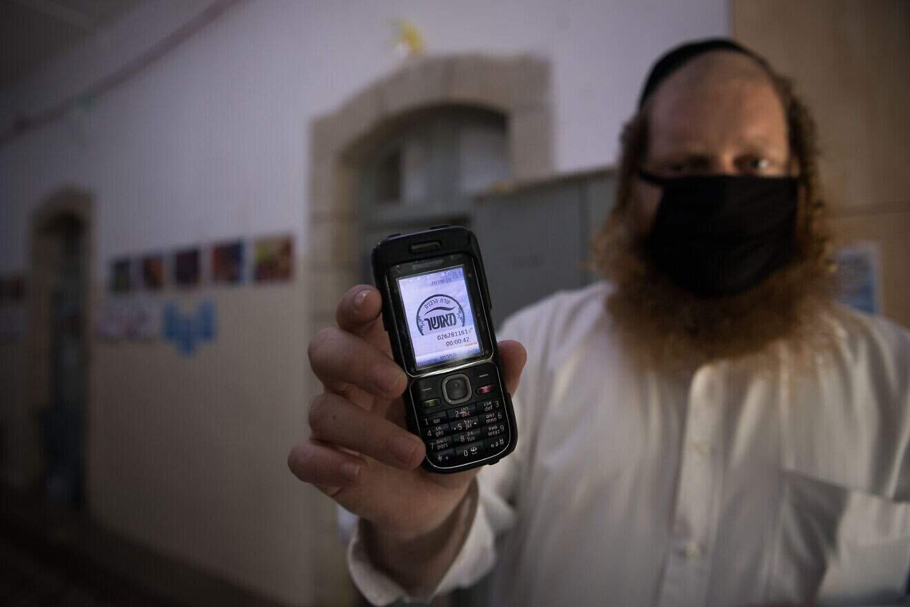 A teacher holds up his cellular phone, certificating that it is a "kosher" one, at the entrance to an ultra-Orthodox school in Jerusalem, May 6, 2020. Photo by Nati Shohat/Flash90.