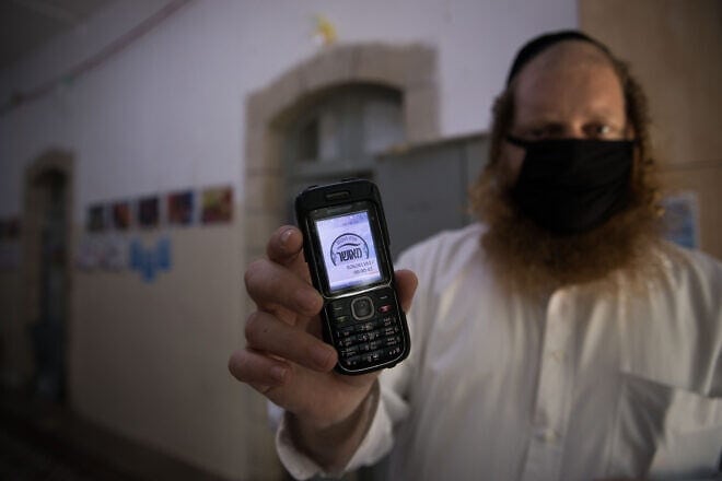 A teacher holds up his cellular phone, certificating that it is a "kosher" one, at the entrance to an ultra-Orthodox school in Jerusalem, May 6, 2020. Photo by Nati Shohat/Flash90.