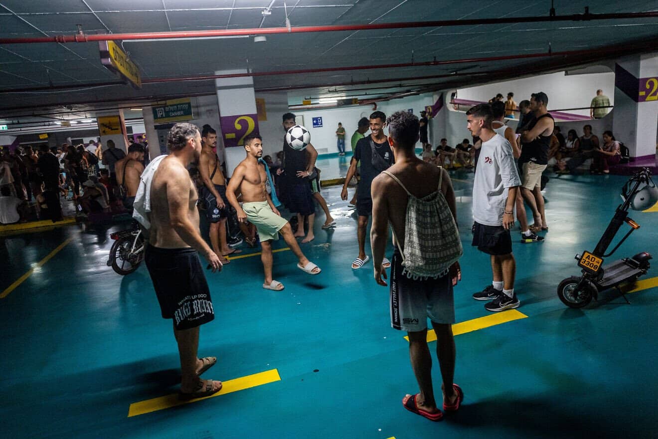 Israelis take cover as siren warns of incoming missiles fired from Iran, at a public parking lot in Tel Aviv, June 18, 2025. Photo by Chaim Goldberg/Flash90.