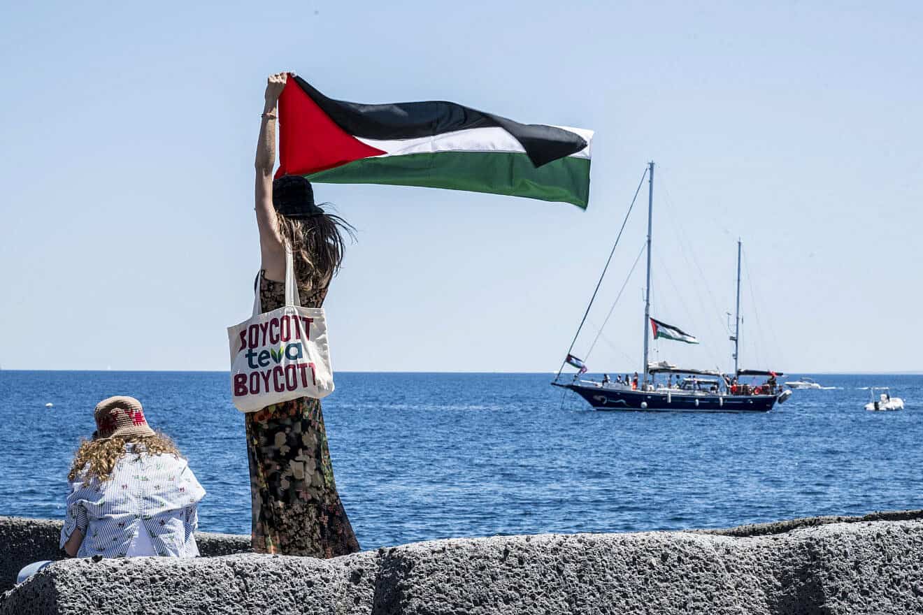 On the quay of San Giovanni Li Cuti, a woman raises the Palestinian flag shortly before the “Madleen” set sail for Gaza in Catania, Italy, June 1, 2025. Fabrizio Villa/Getty Images.