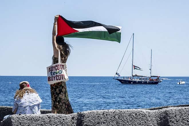 On the quay of San Giovanni Li Cuti, a woman raises the Palestinian flag shortly before the “Madleen” set sail for Gaza in Catania, Italy, June 1, 2025. Fabrizio Villa/Getty Images.