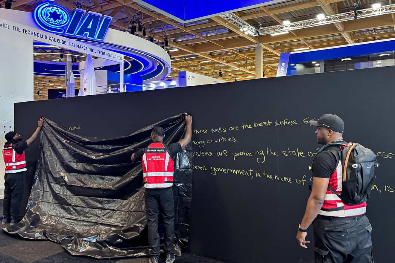Security personnel work to hide graffiti on a panel outside the Rafael booth next to the Israel Aerospace Industries (IAI) at the Israeli Pavillon during the 55th edition of the International Paris Air Show at Paris-Le Bourget Airport on June 16, 2025. France blocked access to the stands of Israeli arms manufacturers for displaying "offensive weapons." Photo by Mathieu Rabechault/AFP via Getty Images.