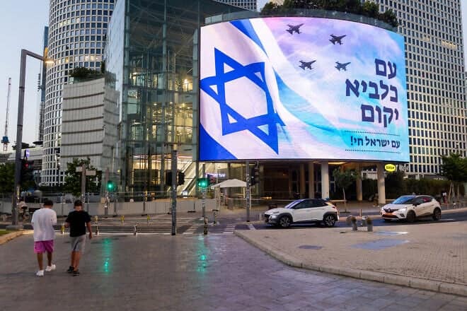 People outside the Kirya military headquarters in Tel Aviv walk past a billboard bearing the name of the Israel-Iran war, June 19, 2025. Photo by Chaim Goldberg/Flash90.
